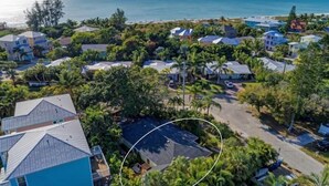 An aerial view of a coastal residential area with houses, palm trees, and a beach in the background.