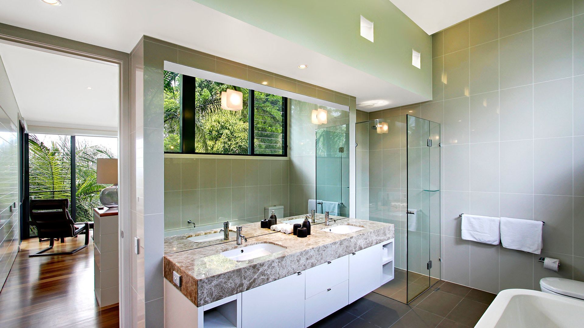 Une salle de bain moderne dotée d’un grand miroir, de deux vasques et d’une douche à parois de verre.