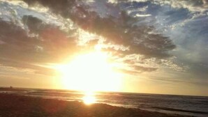 A beach with the sun setting over the horizon.