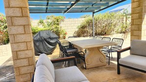 An outdoor patio with a covered table and chairs, brick walls, and a view of the surrounding garden.