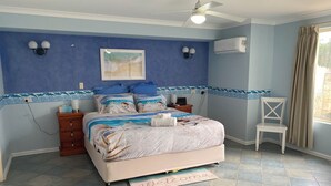 A bedroom with a bed, a chair, a ceiling fan, an air conditioner, and a welcome mat.