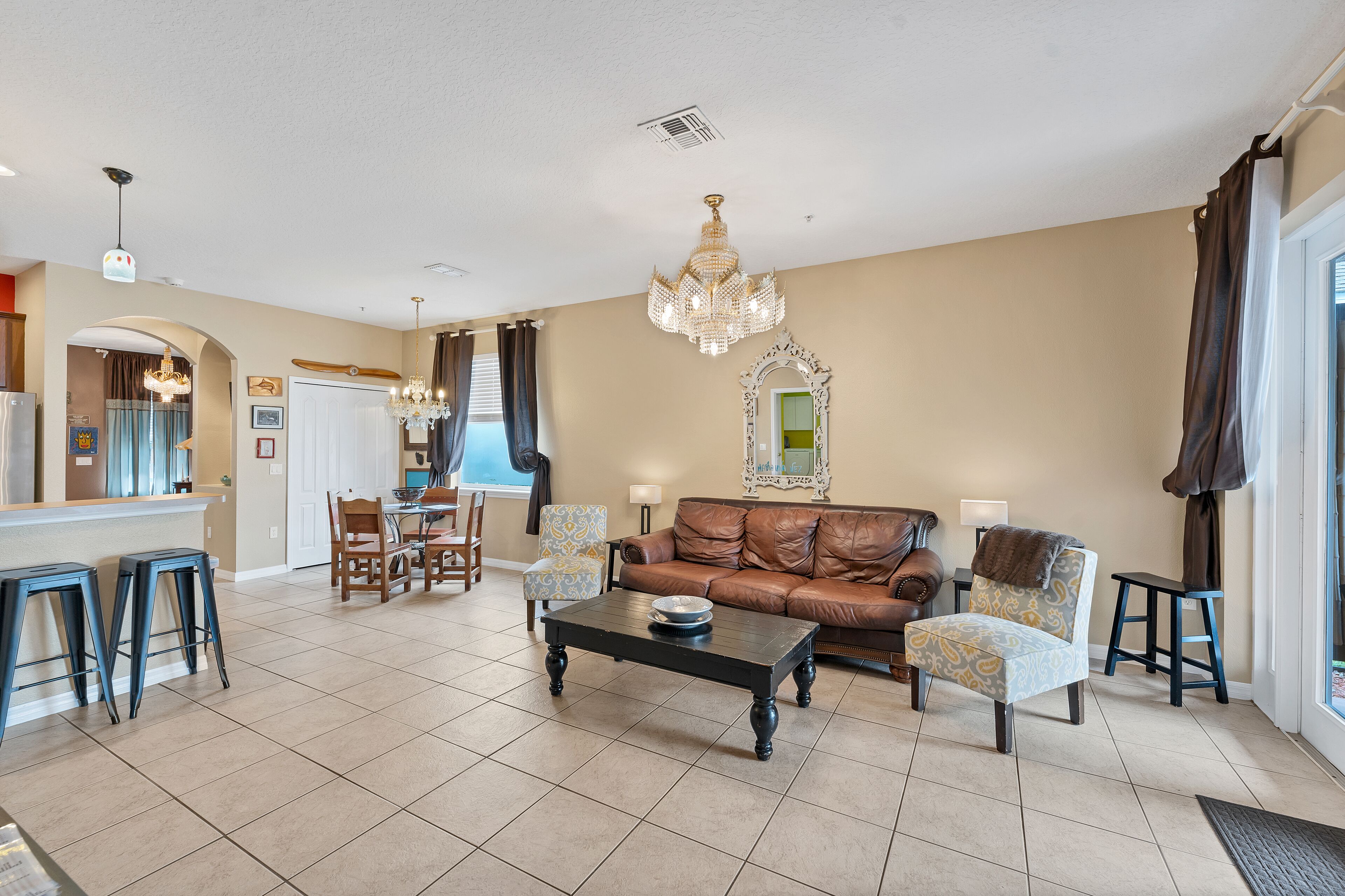 A spacious living room with a brown leather sofa, a coffee table, and a dining area with a kitchen in the background.