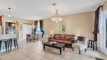 A spacious living room with a brown leather sofa, a coffee table, and a dining area with a kitchen in the background.