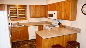 Une cuisine avec des meubles de rangement en bois, un four à micro-ondes, une cuisinière et deux tabourets.
