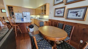 A kitchen with wooden cabinets, a refrigerator, a sink, and a dining area with a wooden table and chairs. - Snowcreek Resort Vacation Rental 985 (Mammoth Lakes)