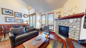 A living room with a stone fireplace, leather sofa, wooden coffee table, and a dining area with a bench and chairs.