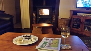 Ett mysigt vardagsrum med en öppen spis, en tv, ett bord med ett glas vin och en tallrik mat.