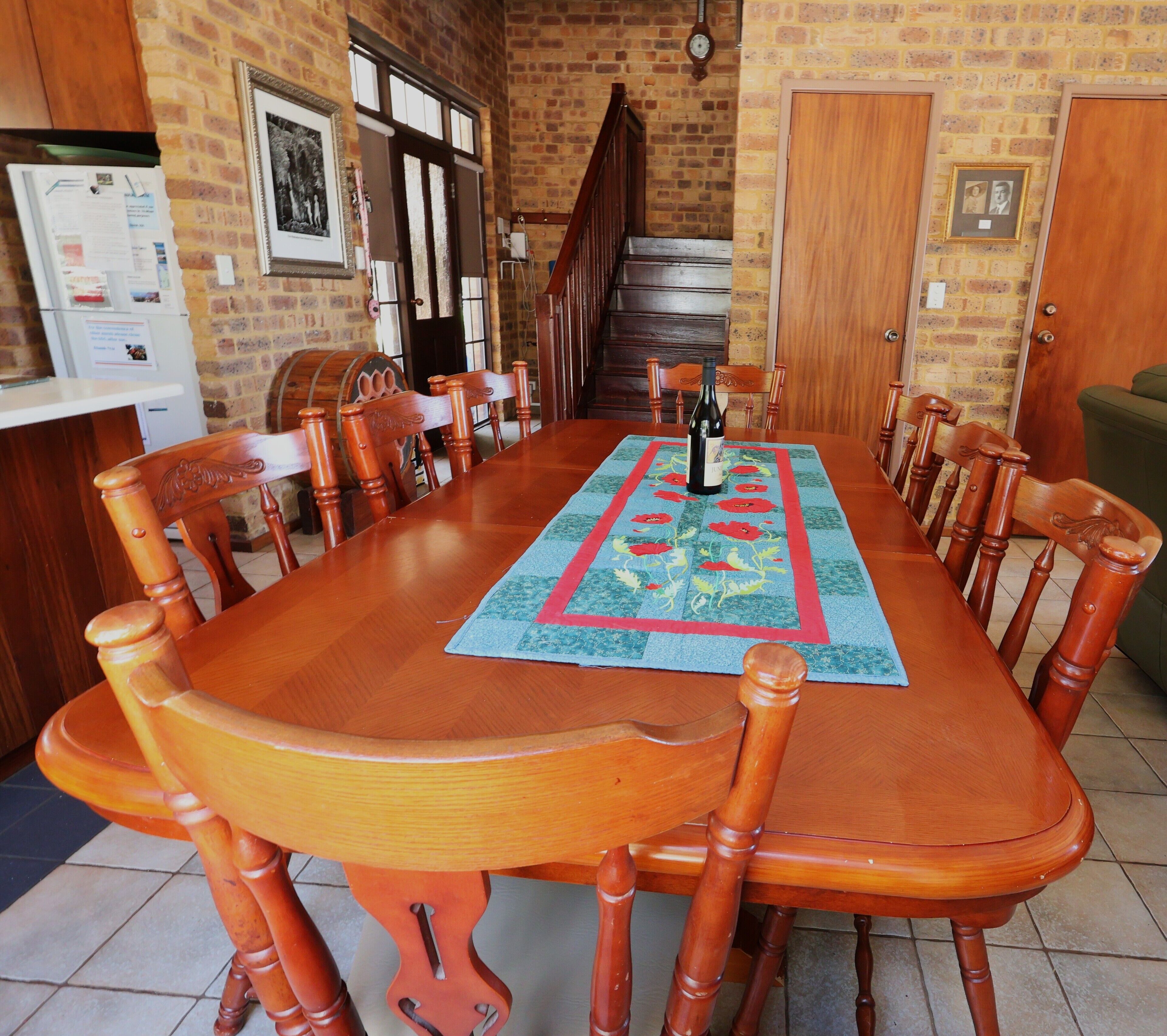 A dining area with a long wooden table, chairs, a rug, and a bottle of wine.