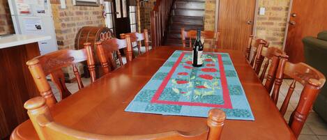 A dining area with a long wooden table, chairs, a rug, and a bottle of wine.