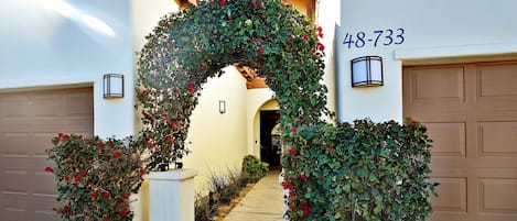 Una entrada de casa con un arco decorativo cubierto de follaje y flores rojas, que lleva a un garaje con el número 48-733.