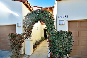 A residential driveway with a decorative archway covered in foliage and red flowers, leading to a garage with the number 48-733.