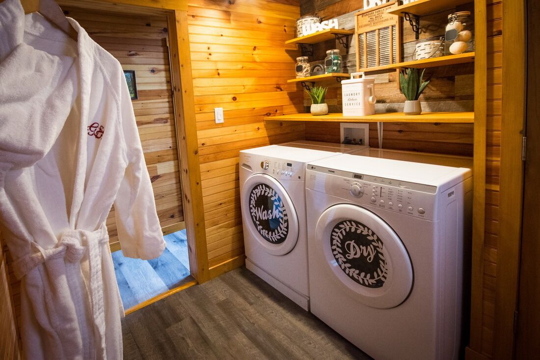 A laundry room with two front-loading washing machines, wooden walls, and shelves with various items.