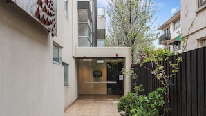 A narrow alleyway with a building entrance, a glass door, and a wooden fence. - Lalique Elwood Beachside Apartment (Elwood)