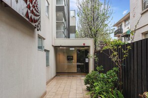 A narrow alleyway with a building entrance, a glass door, and a wooden fence. - Lalique Elwood Beachside Apartment (Elwood)