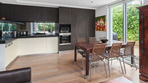 A modern kitchen with a dining area, large windows, and a view of greenery. - Lalique Elwood Beachside Apartment (Elwood)