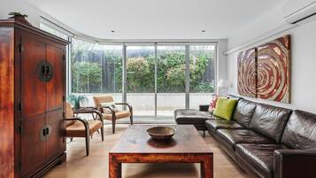 Relax in this stylish living room with a leather sofa, armchairs, and a coffee table, offering a view of lush greenery outside.