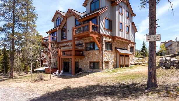 Ein mehrstöckiges Haus mit Steinverkleidung, Holzbalkonen und einem Hinweisschild für das Skigebiet.