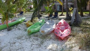 Several inflatable kayaks on a sandy beach with palm trees and a building in the background. - Exuma's best kept secret (Rolleville)