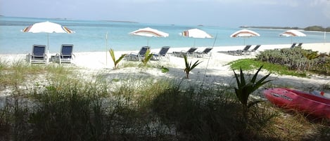 A beach with white umbrellas and lounge chairs, a red kayak, and clear blue water.
