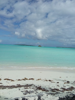 Une plage à l’eau turquoise et limpide, un rivage sablonneux et une petite île qui se profile à l’horizon.