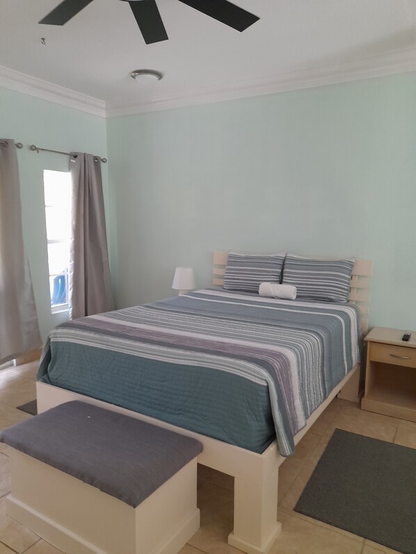 Ein Schlafzimmer mit einem Bett, Nachttischen, einem Fenster mit Vorhängen und einem Deckenventilator.