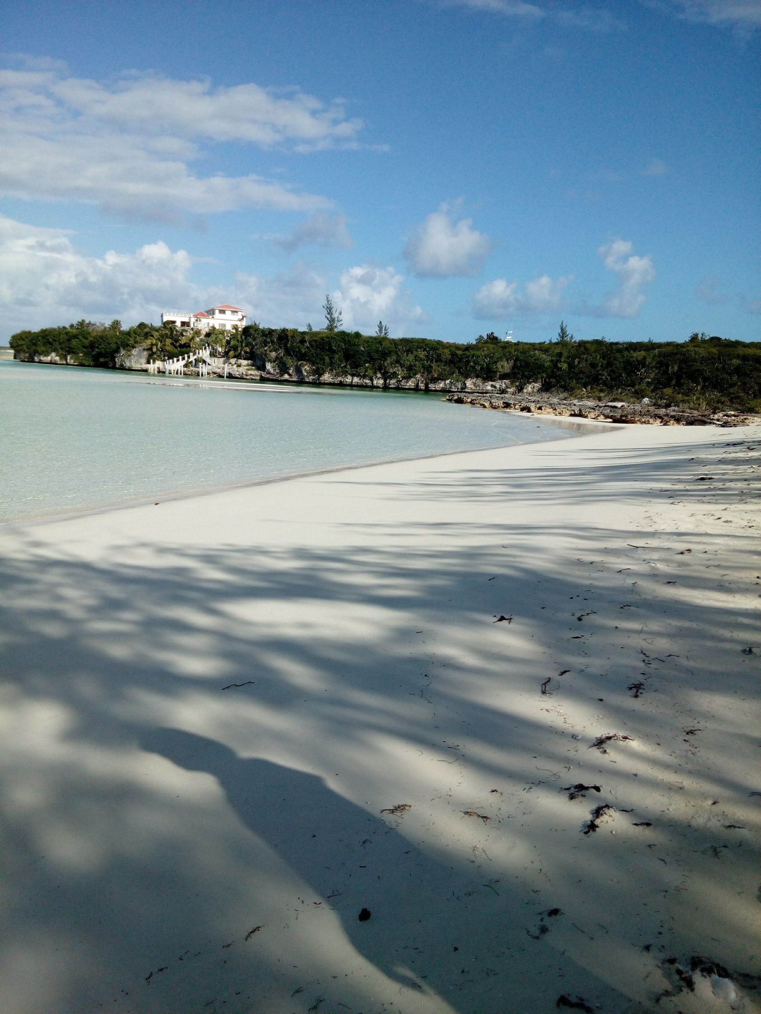Ein Strand mit klarem Wasser, weißem Sand und einem weißen Gebäude auf einer kleinen Insel.