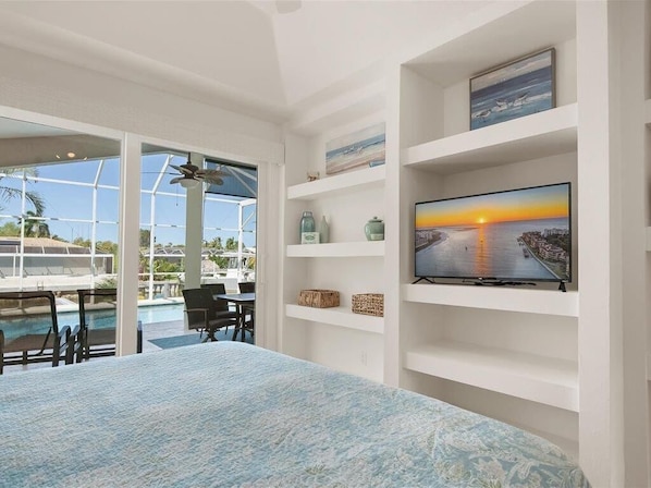 A room with a large bed, a TV on a white shelf, a pool view, and a ceiling fan. - Waterfront 3BR Marco Island home with heated pool and free WiFi. (Marco Island)