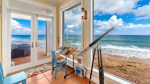 Una stanza con una grande finestra vista spiaggia, un telescopio e un tavolo con libri e giochi.