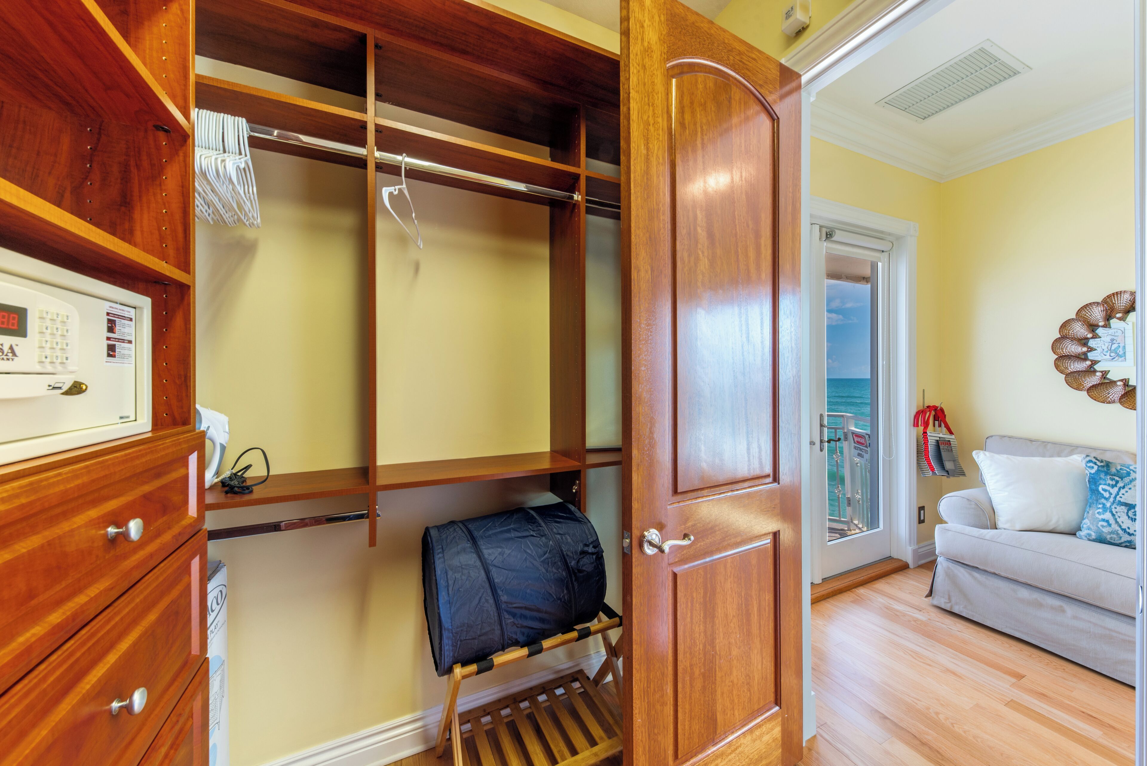 A room with a wooden wardrobe, a small desk with a telephone, and a view of the sea through a door.