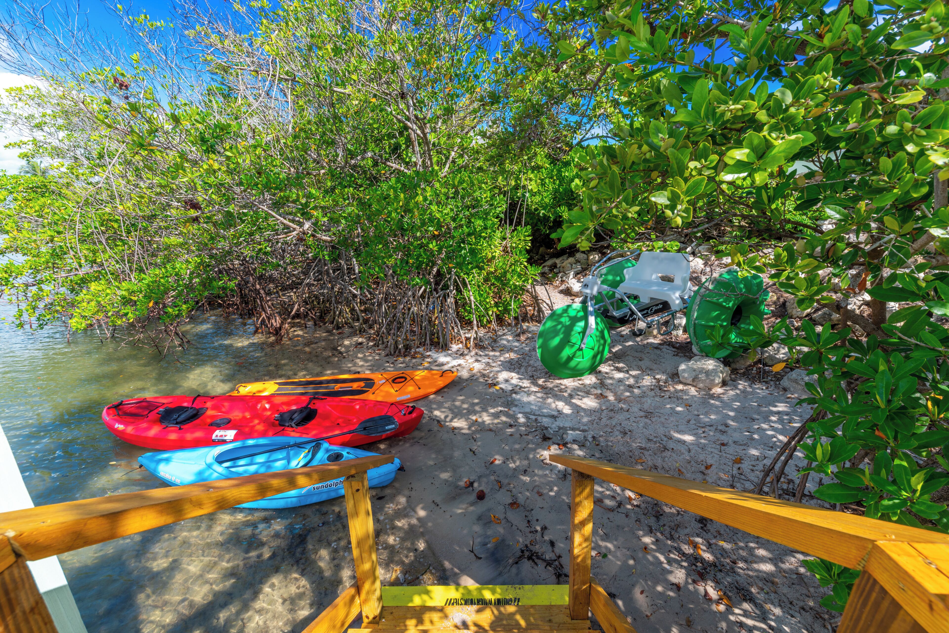 Zona de almacenamiento de kayaks en la playa, con kayaks y una bolsa verde.