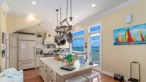 Una cucina con una grande isola, sgabelli da bar bianchi e vista sull'oceano.