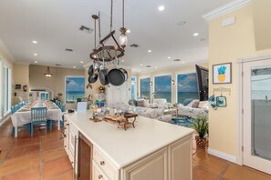 A spacious kitchen with a large island, overhead pot rack, and a view of the ocean through the windows.