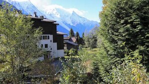 Uma pousada de montanha com design moderno, cercada por vegetação exuberante e picos nevados ao fundo.