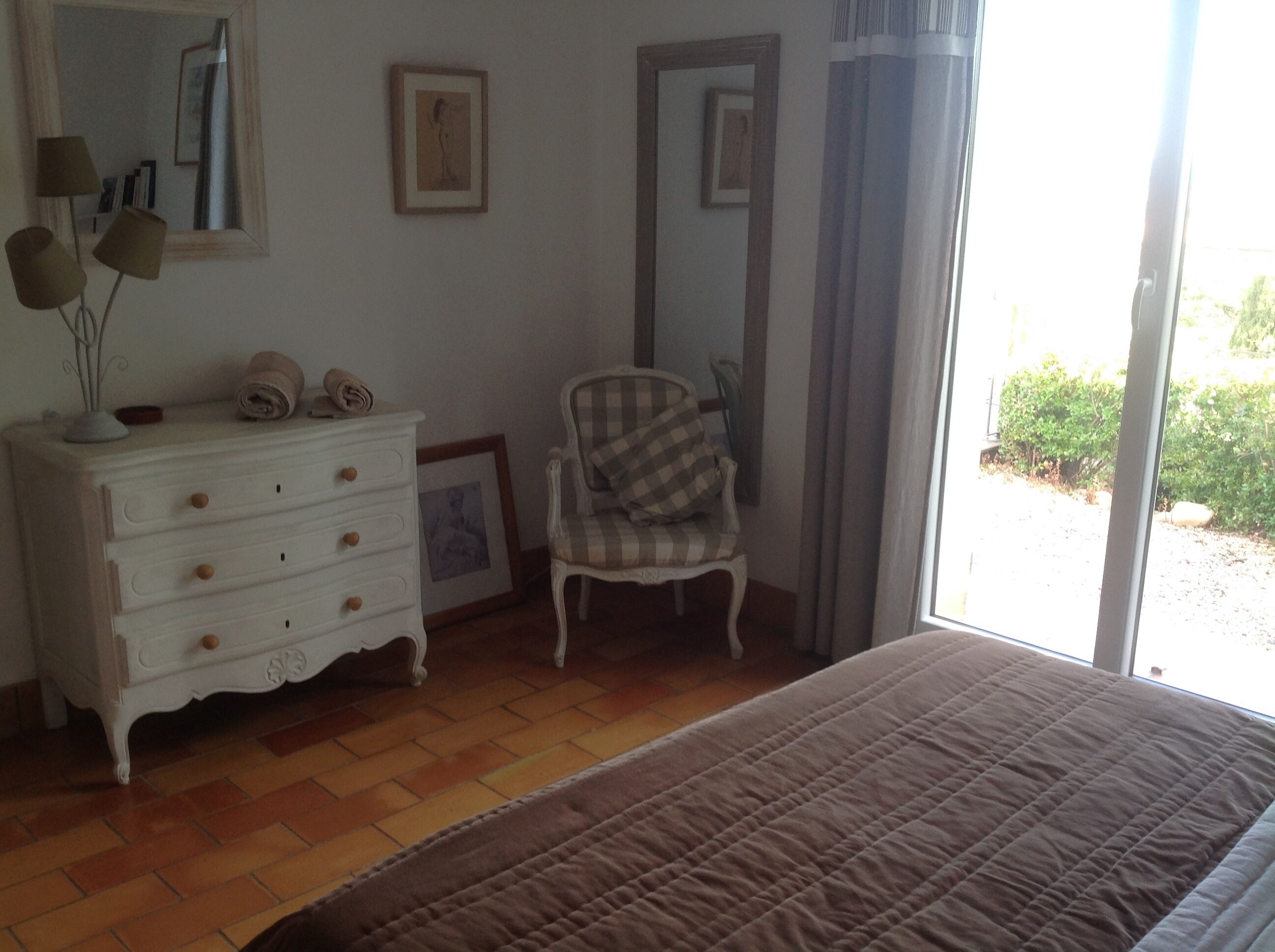 Une chambre à coucher avec un lit, une commode, une chaise et une fenêtre avec des rideaux.