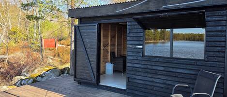 A cabin with a deck, a chair, and a window overlooking a body of water.