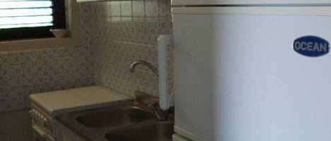 A compact kitchen with white cabinets, a stainless steel sink, and a white refrigerator with a blue logo.
