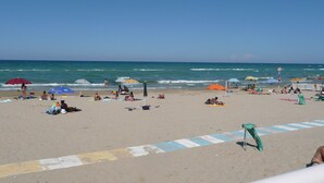 Une plage où des gens se détendent sous des parasols, un ciel dégagé et l’océan en arrière-plan.