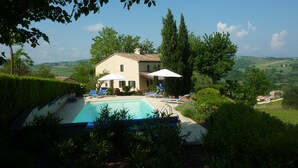 Une maison avec une piscine, entourée de verdure et de collines.