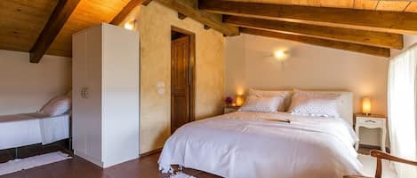 A bedroom with a large bed, a smaller bed, and a wardrobe. There is a wooden ceiling and a door leading to another room.