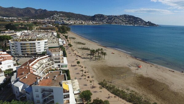 A coastal town with a beach, buildings, and mountains in the background. - Amazing apartment on the seafront in Roses Inmosantos Oasis B7 (Rosas / Roses)