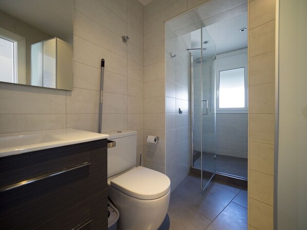 A modern bathroom with a toilet, a glass shower enclosure, and a vanity with a mirror. - Amazing apartment on the seafront in Roses Inmosantos Oasis B7 (Rosas / Roses)