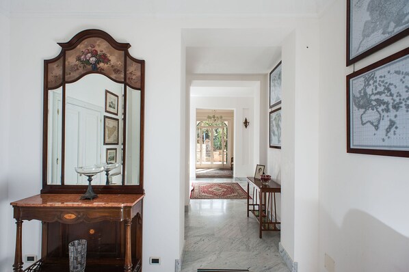 Un pasillo con piso de mármol, una mesa de madera con un florero y un espejo grande.
