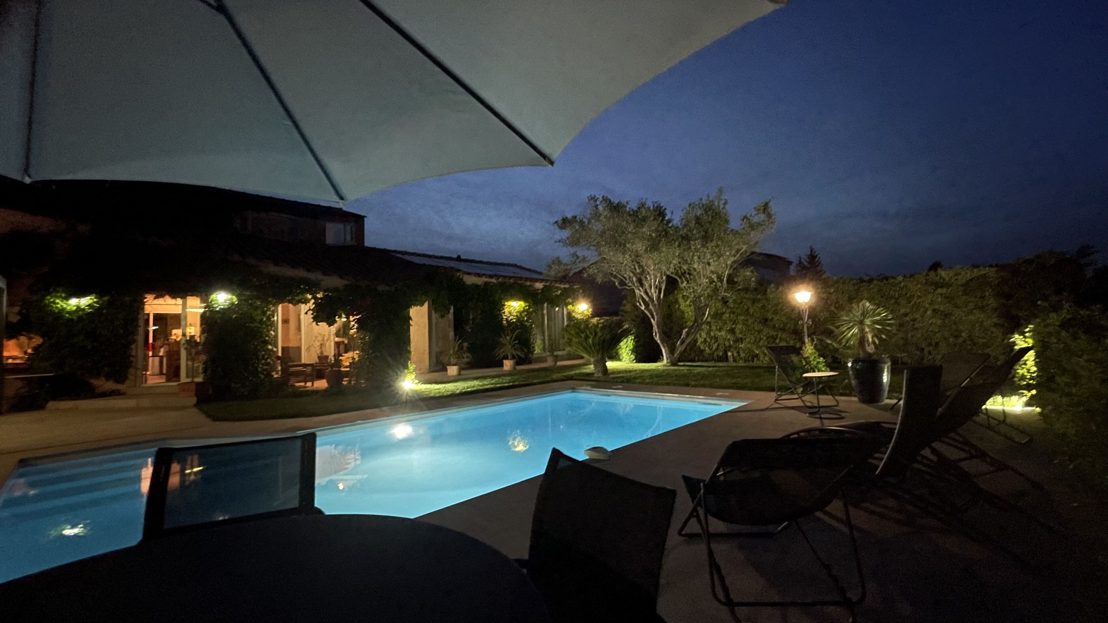 An outdoor swimming pool area with a covered seating area and a house in the background.