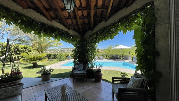 Uma área de varanda coberta com piscina, móveis de jardim e vegetação exuberante.