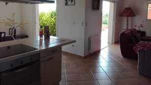 Una cucina moderna con una grande isola, un'area pranzo con un divano rosso e vista sul verde circostante.