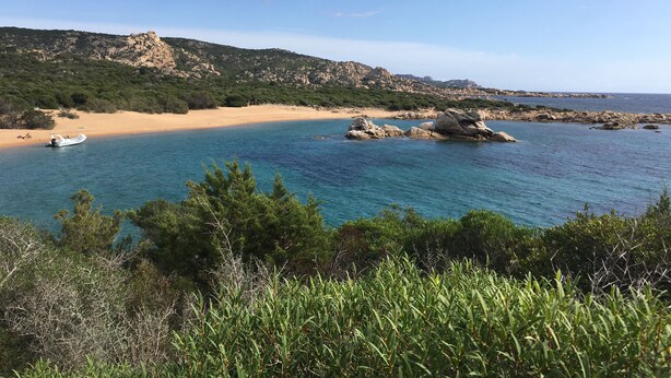 Paesaggio costiero con spiaggia sabbiosa, affioramenti rocciosi e acque cristalline.