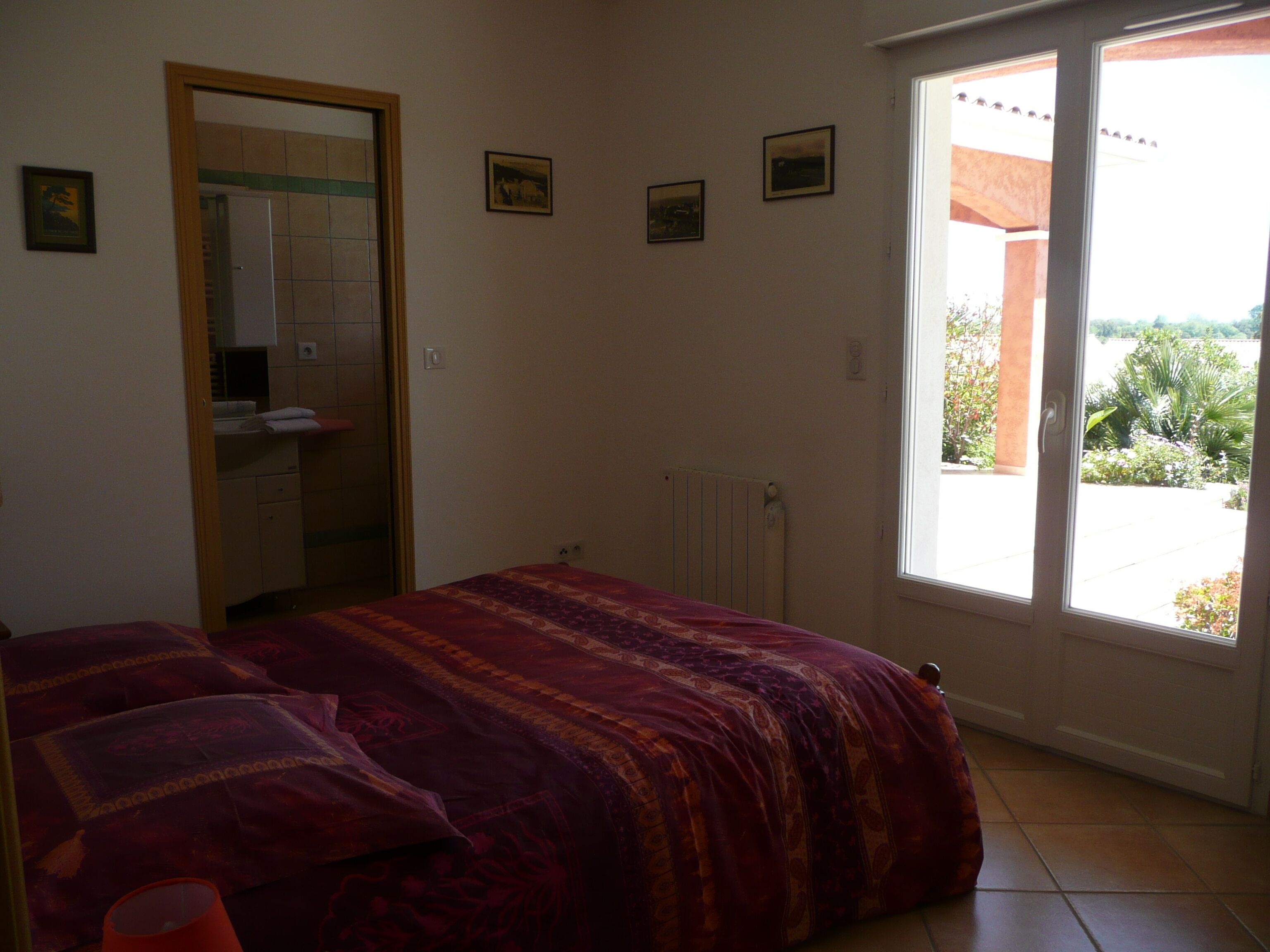 A bedroom with a bed, a radiator, a window with a view, and a door leading to a bathroom.