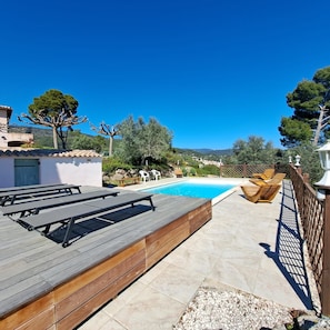 Ein Poolbereich mit Holzterrasse, Liegestühlen und freiem Blick auf die umliegende Landschaft.