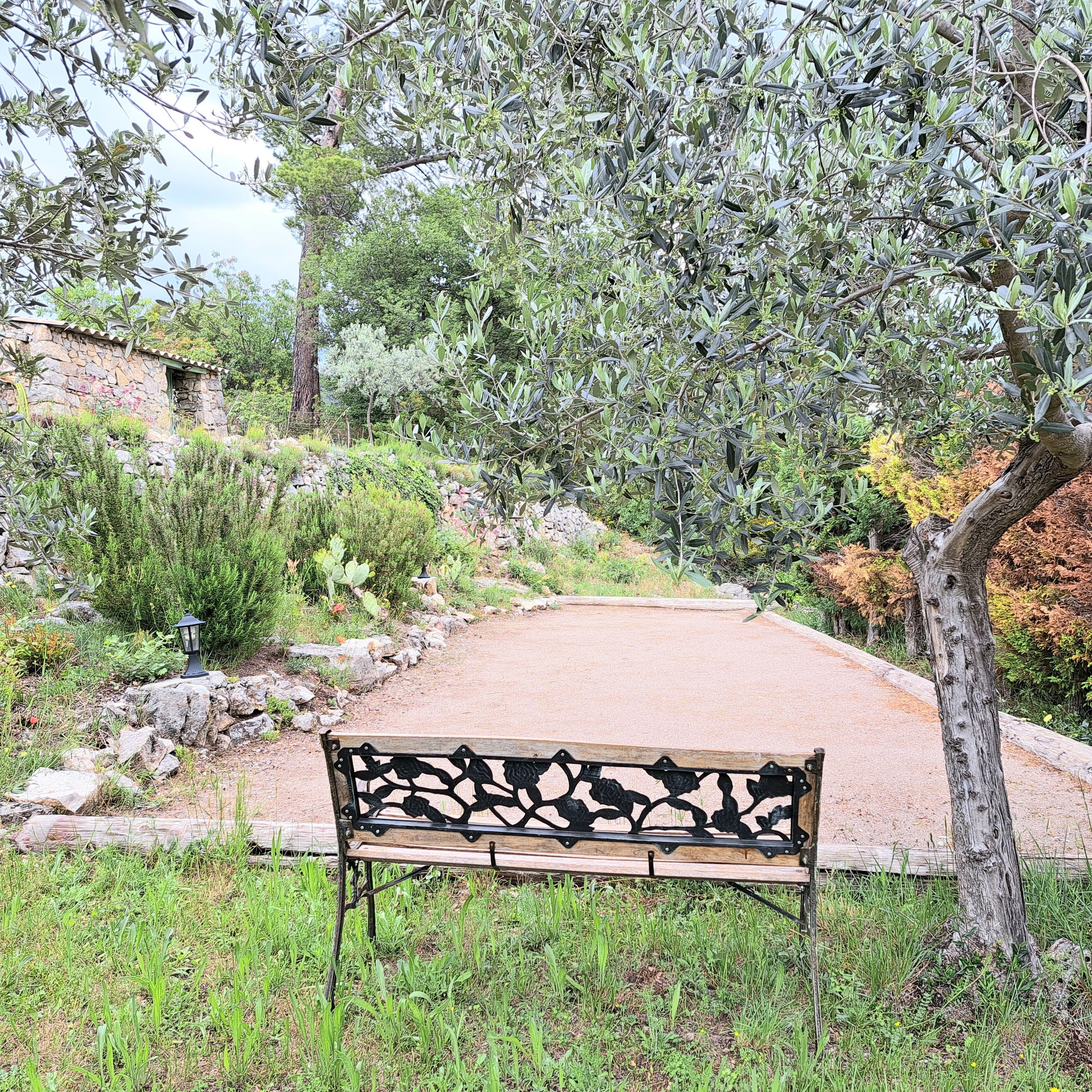 A bench in a garden with a stone wall and trees.