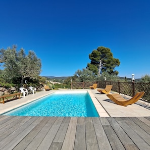 Ein Schwimmbad mit Holzterrasse, Liegestühlen und Blick auf die Landschaft.